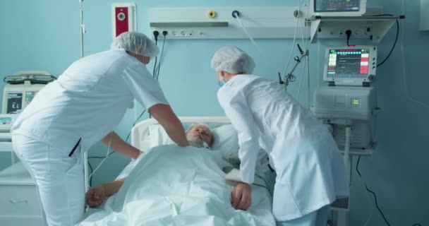 躺在医院病床上的昏迷不醒的老人护士跑到病人身边 医护人员跑来跑去帮助垂死的病人 躺在医院急诊室的床上 — 图库视频影像