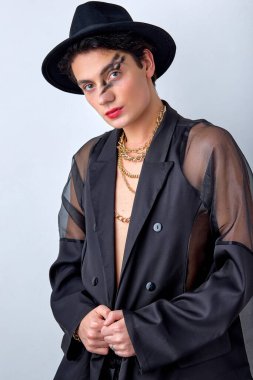 Şık transseksüel erkek LGBTQ beyaz arka planda izole edilmiş muhteşem bir tavırla ve özgüvenle poz veriyor. Siyah giysili ve şapkalı beyaz bir adam. moda konsepti