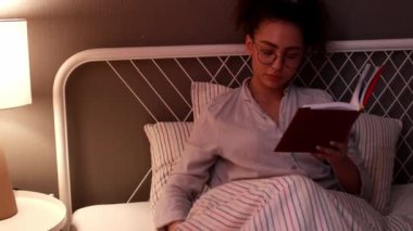 At kuyruklu güzel esmer kadın gece yatakta kitap okuyor, günlük rutin, yaşam tarzı, hobi, yakın çekim, kamera hareketi, eğitim yavaş çekim.