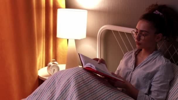 Νεαρή Γυναίκα Διαβάζει Βιβλίο Πριν Κοιμηθεί Κλείνοντας Βιβλίο Βγάζοντας Γυαλιά — Αρχείο Βίντεο