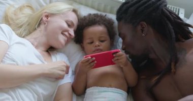 Kafkasyalı karısı ve Amerikalı kocası online oyunlar oynayan, yatak odasında uzanan sevimli küçük kızını öpüyor Aşk İlişkisi, Yavaş çekim mutluluk hobisi, ilgi çekici