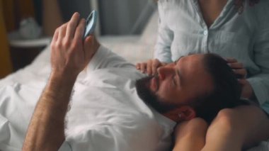 Mutlu romantik çift yatak odasında akıllı telefonuyla selfie çekiyor. Erkek ve kadın yatakta fotoğraf çekmek için cep telefonu kullanıyor. Aile video görüşmesi yapıyor, yavaş çekimde sohbet ediyor.