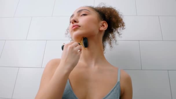 年轻的高加索美女在蓝色的顶部 文胸使用面部辊在浴室 女孩在家里按摩脖子 享受免费的业余时间 健康和身体护理 — 图库视频影像
