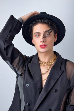 Erkek makyajı. Siyah şık giyinen, şapkalı, yüzünde makyajı olan seksi esmer adamın portresi. Beyaz stüdyo geçmişinden kameraya bakan beyaz bir adam. güzellik, moda konsepti