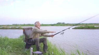 Yaşlı sakallı adam olta atıyor, büyükbaba tek başına balığa çıkıyor, hobi olarak dinleniyor boş zaman aktiviteleri yavaş çekim.