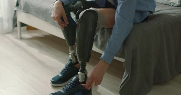 有坚强精神的英俊男人是不会放弃的 截肢后的康复 男人习惯了假肢 穿着运动鞋坐在家里明亮的卧室床上 — 图库视频影像
