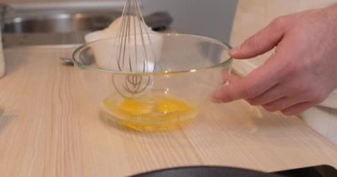 Elinde çırpı tutan bir adam mutfak masasındaki cam kasede yumurta çırpıyor. Turta, tatlı ve krep hazırlama. Kesilmiş manzarayı yavaş çekimde kapat.