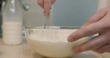 Mutfakta cam kase tutan ve krep hamuru yoğuran bir adam. Kesilmiş yan görüntüyü yavaş çekimde kapat. # Erkek şefin elleri # # karışımı karıştırıyor malzemeleri # # çırparak kaseye #