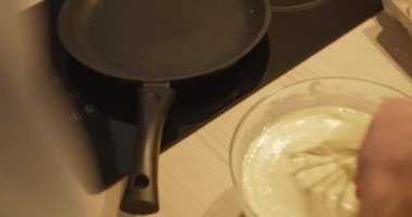 Genç sakallı adam hamur işi yapıyor, parmağını kaseye sokuyor, tadıyor, yakından bakıyor, adam hamur işlerinden zevk alıyor.