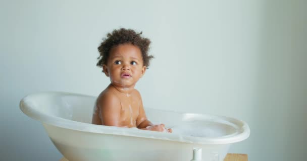 严重有趣的美国黑人孩子在白色的浴室洗澡 女孩一个人在浴缸里洗澡 在家里 在周末的早上 快乐健康的男孩或女孩玩耍 泼水和玩乐 — 图库视频影像
