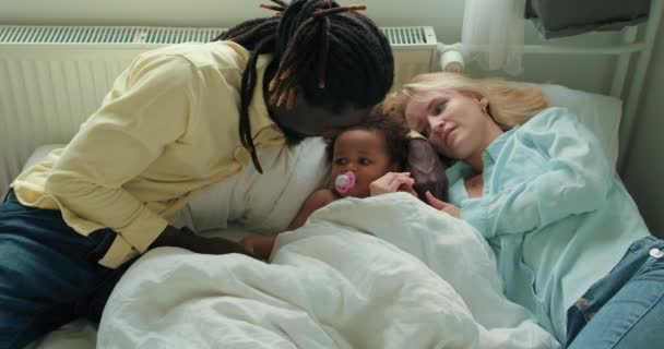 家庭团聚时间 非裔美国人和白人父母 女儿躺在床上 快乐的国际家庭躺在客厅慢动作爱情关系生活方式 — 图库视频影像