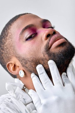 Closeup portrait of black man with make-up touching face head, in white gloves, elegant and gorgeous male in white shirt posing as professional model, looking feminine or womanlike, princess, cute clipart