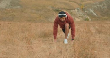 Genç adam başlangıç pozisyonunda, açık havada kardiyo performansı ve maraton koşuyor. Spor, dağlar ve erkek koşucuyla egzersiz ve spor, ırk ve özgürlük eğitimi.
