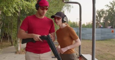 Skeet Atış Sporu. Çiftler eğlence ya da spor amaçlı yavaş çekim yapmak istiyor. Sportmenlik. Yakışıklı beyaz adam ve genç kadın silah eğitimi almadan önce silahların detaylarını kontrol ediyorlar.