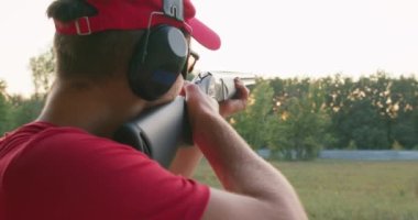Skeet Atış Sporu. Genç yetişkin bir adam roket yarışması sırasında ateş ediyor, nadir bir manzara. Adamın biri pompalı tüfekle atış yapıyor. Silahlı adam asfalt güvercini vuruyor.