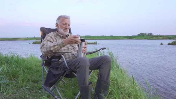 古い疲れた漁師が休憩し 釣りのアウトドア中に休息し 魔法瓶を持ち 熱いお茶を飲み 時間を楽しみ 休日を楽しみ 引退し ライフスタイルの平和と静かな喜びの幸福レジャー — ストック動画