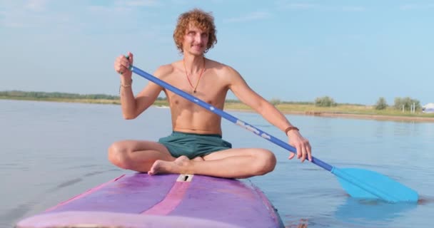 快乐快乐的人 夏天坐在浅滩上 船桨划过美丽的大海 蓝蓝的天空 快乐的高加索男性冲浪者度假时享受户外生活和水上运动 — 图库视频影像