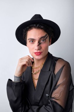 Siyah yarı şeffaf gömlekli, şapkalı, beyaz stüdyo arka planında kameraya poz veren seksi bir kadın. Zincirli, parlak parti makyajlı, tutkulu ve şehvetli görünen yakışıklı bir adam.