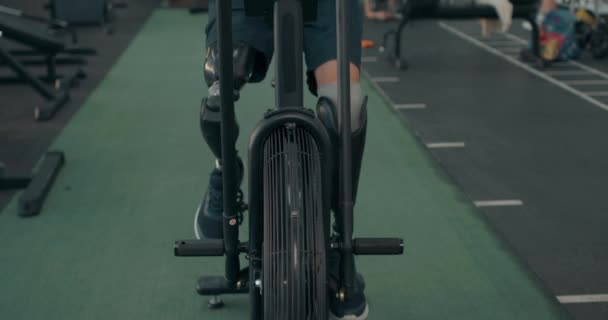 ジムで回転自転車を使用して生体の足を持つ筋肉の男スローモーション スポーツマンは ジムクロスフィットで心臓トレーニングセッションに参加 — ストック動画