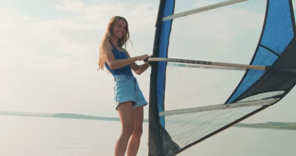 美しい笑顔の女の子サーフィンには 帆を保持し 旅行から喜びを得る学習されます 冒険自由時間ライフスタイルスローモーション 真夏の休暇中に湖でウィンドサーフィンに乗っているブロンドの女性 — ストック動画