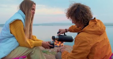 Birlikte kamp yapacağız. Turist çift, kamp ateşinin yanında oturan erkek kadın termostan çay içiyor. Turizm, mutlu ilişkiler aktif yaşam tarzı spor giyimli evli çift dinleniyor, dinleniyor.