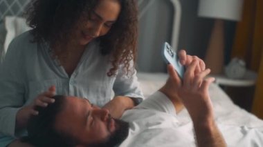 Gülümseyen güzel bir kadın kocasının kafasını okşuyor, onunla ilgileniyor, adam karısının dizlerinin üstünde yatıyor. Bacaklar internette sörf yapıyor, yavaş çekimde alışveriş yapıyor.