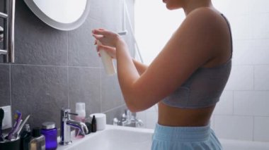 Duştan sonra banyodaki güzel kız biraz nemlendirici krem kullanarak aynaya bakıyor. Yüzüne ve boynuna uyguluyor. Yavaş çekim sağlığını ve vücut bakımını kapatıyor.