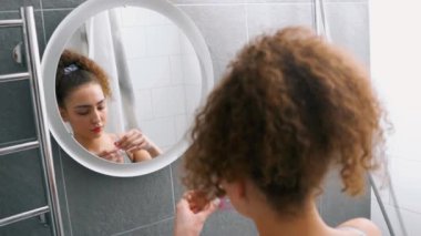 Güzel, ciddi bir kadın aynaya bakıyor, banyoda göz bandı yapıştırıyor, ağır çekimde. Kaliteli zaman, yaşam tarzı, ev hayatı aynanın sağlığını yansıtır.