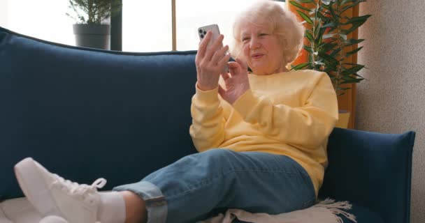 Fröhliche Seniorin Ruht Sich Auf Sofa Aus Tippt Auf Smartphone — Stockvideo