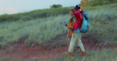 Neşeli mutlu çift güneşli bir günde spor yapmak için dağ yolunda yürüyüş yapıyor. Aktif insanlar, bastonlarıyla kayalık yolda sırt çantasıyla geziyorlar. Aile bir macerada, doğayı keşfetmekten zevk alıyor.