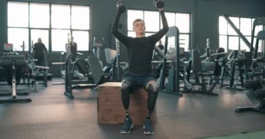 Engelli genç adam kafasının üzerine halterleri kaldırıyor, sporcu egzersizi yapıyor, spor salonunda halterlerle göğüs egzersizi yapıyor, rehabilitasyon sırasında dambıllarıyla kollarını uzatıyor.