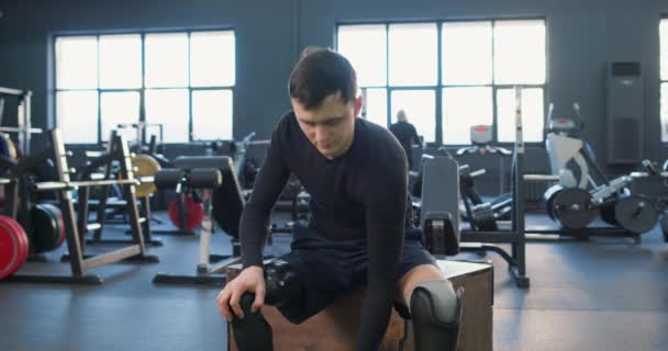 年轻健康 精力充沛 有野心的残疾人 在健身房接受哑铃训练 运动健将 双腿灵巧 坐在盒子上 肌肉男 交叉配合 — 图库视频影像