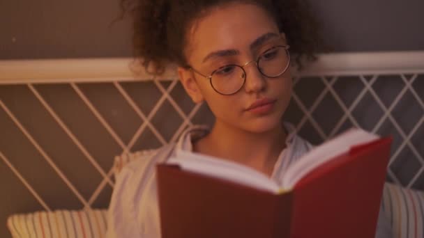 漂亮的女学生专心致志地准备考试 阅读日记 让她想起童年时代 戴眼镜的女孩把书签放进书本 关上书本 躺在床上慢镜头 — 图库视频影像