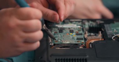 Demir lehim tutan ve lehimleyerek devre levhasını tamir eden tanınmamış bir adam. Elektrik işi konsepti. Ağır çekim. Genç adam atölyesinde elektronik devreler üzerinde çalışıyor.