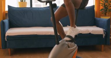 Siyah, genç, seksi, kaslı, çıplak vücutlu bir adam evde bisiklet sürüyor, antrenman yapıyor. Gömleksiz, bacaksız, bisiklet üstünde kardiyo antrenmanı yapan bir adam. spor, sağlıklı yaşam tarzı konsepti