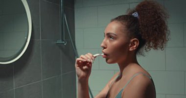 Ciddi bir kız, modern iç dekorasyonla banyoda dişlerini fırçalamaya odaklanmış. Bayan öğrenci üniversiteye gitmeden önce su prosedürlerini uyguluyor.