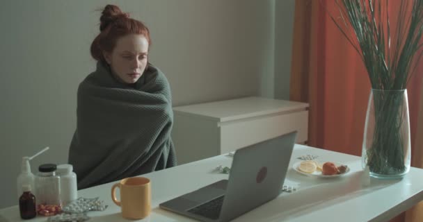 映画を見ながら毛布に包まれた病気の赤い髪の女性は ラップトップで作業し 医師とオンラインで相談していますビジネススローモーションフリーランサー — ストック動画