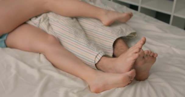 陽気な女の子と夫がベッドで楽しそうに笑っている女性が彼氏の体に脚をつけて — ストック動画