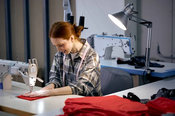 Textile cloth factory working process tailoring modern clothes, young beautiful caucasian woman at work, engaged in tailoring using modern sewing machine. dressmaker enjoy sewing, tailoring