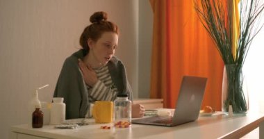 Kızıl saçlı, soluk benizli, zayıf bir kadın, doktorla, görüntülü konuşma, arkadaşla konuşma, çay içme, hap alma, öksürük, sohbet teknolojisiyle çevrimiçi video görüşmesi yapıyor.