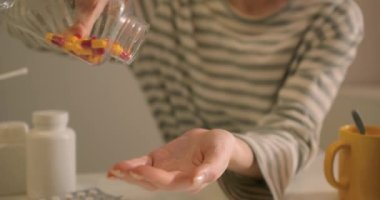 Kadın eli kapsülleri ilaç şişesinden eline döken yakın plan. Hasta günlük ilaçlarını tüketiyor. Kadın eli, şişeden dökülen günlük ilaç haplarından alıyordu.