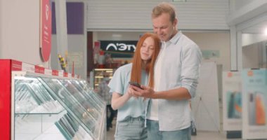 Mutlu gülümseyen adam ve kadın ellerinde son model telefon, teknoloji, kontrol, test, ağır çekim, teknolojik alışveriş aleti konsepti. Mobil dükkanından yeni bir akıllı telefon alan mutlu gençler.