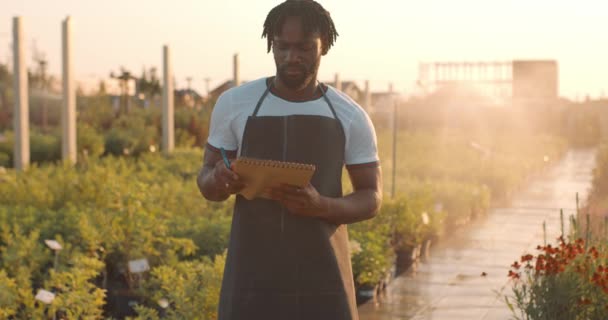 Ciddi Siyah Düşünceli Işçi Notlar Alıyor Arka Planda Bitkiler Sulanıyor — Stok video