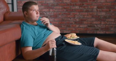 Çıplak karnına uzanmış TV seyreden tombul bir çocuk. Yavaş çekim. Çocuk obezitesi üreten ergen evde dinleniyor.