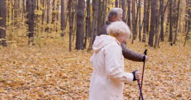 Yaşlı neşeli adam ve kadın turistler ormanda çubuklarla yürüyüş yapıyorlar. Olgun çiftlerin aktif istirahatı, boş zaman yavaş çekim, yan görüş, ortak ilgi alanları, romantik randevu, sağlık ve vücut bakımı.