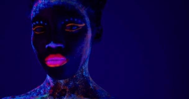 黑色严肃的女士 身体艺术在紫外光下发光 漂亮的女人脸上涂满了荧光粉 与世隔绝的深紫色空间 时尚的概念 美容业 美容业 — 图库视频影像