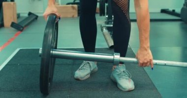 Zayıf formda sporcu kadın spor salonunda halterle egzersiz yapmaya hazırlan, halter plakasını elinde tut. Sporcu kadın spor salonunda halterin üzerine ağır tabaklar koydu..