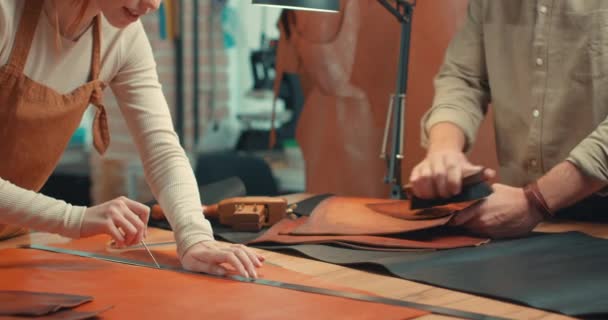 英俊潇洒的男人和红头发的女人一起在一家制造厂工作 女人用圆顶标记一块皮革 男人用清洁的材料慢动作家族企业 — 图库视频影像