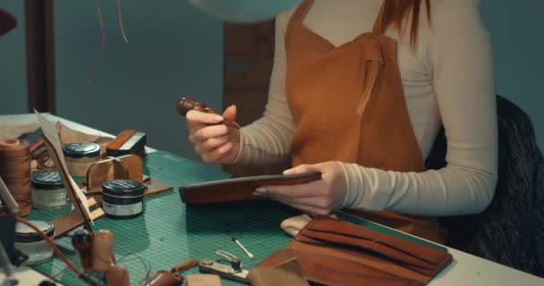 幸せな魅力的なジンジャーテーラーは スライカーで研磨エッジを楽しんで 縫製革手作りの財布レザークラフトを作成し サイドビューの肖像画を閉じます — ストック動画