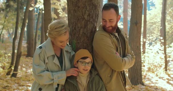 快乐的家庭 男孩散步 秋天在公园休息 家庭假期 周末黄金季节慢动作父母和儿子靠在树上 与可爱可爱的儿子共度温馨的时光 — 图库视频影像